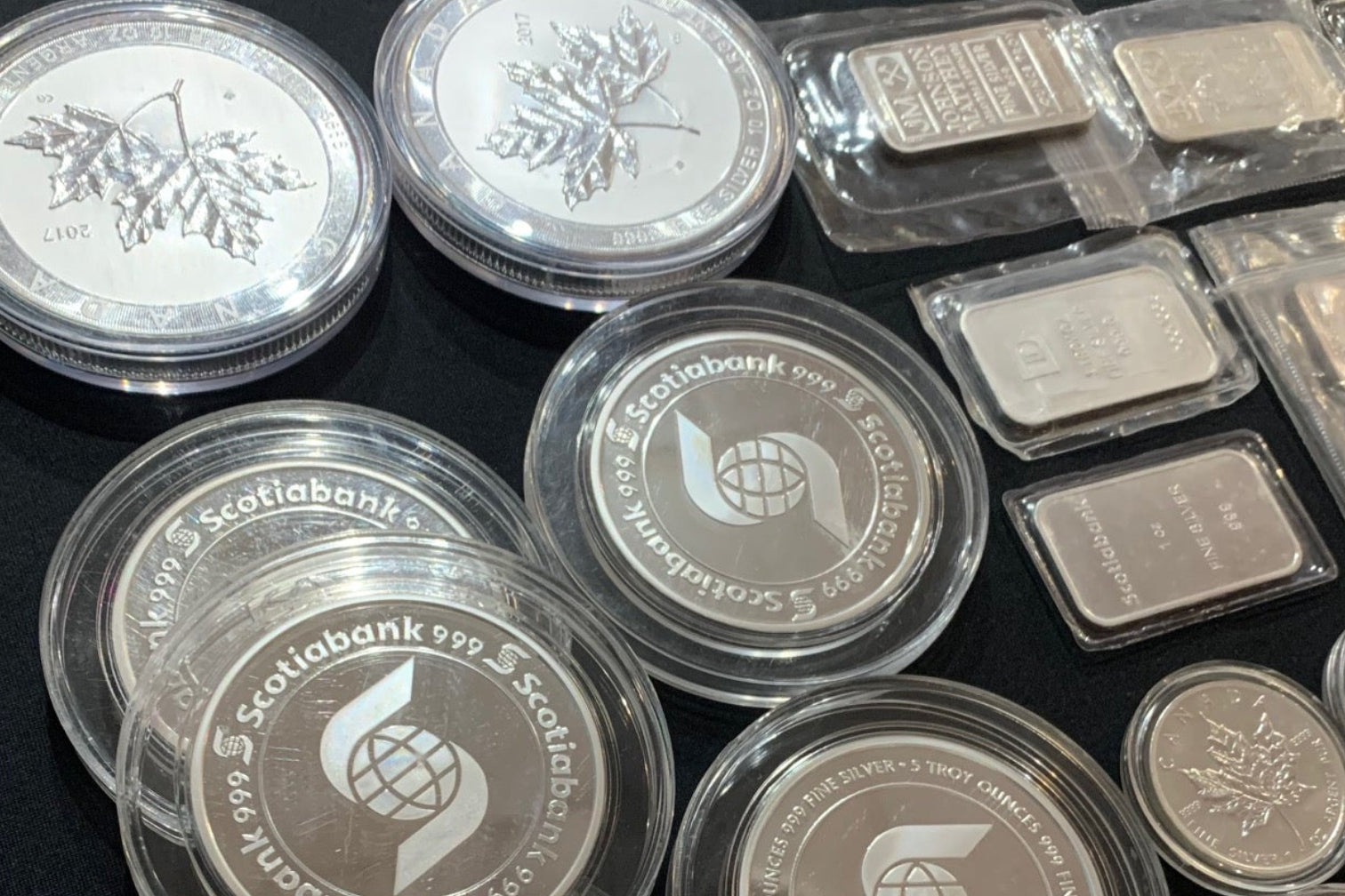 Collection of silver coins and bars with a container on a dark surface